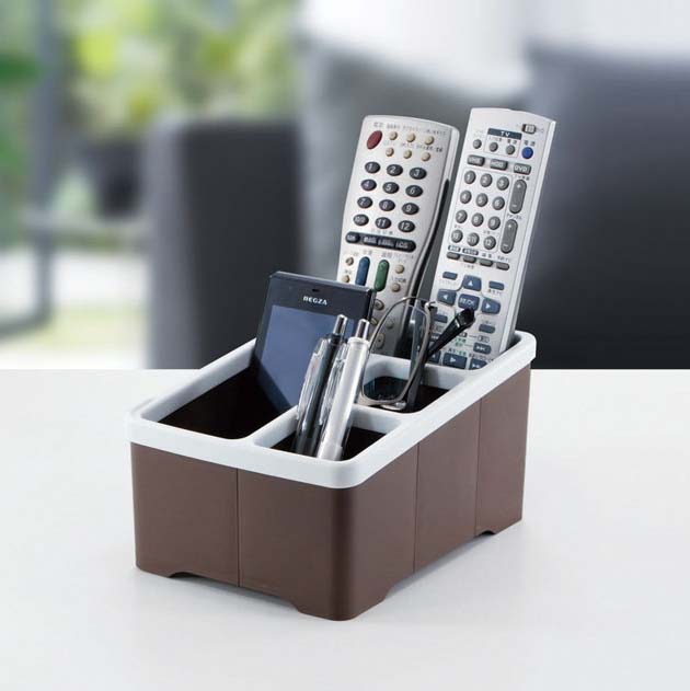A Japan Made brown plastic desktop multipurpose storage box with 2 remote controllers, glasses, and 2 pens.