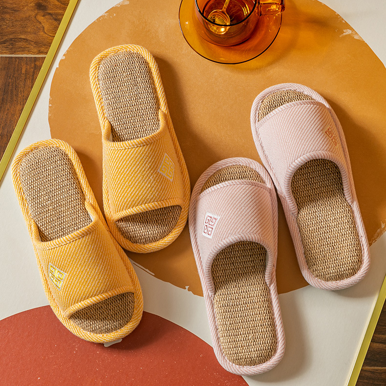 2 pairs of comfortable slippers. The yellow slipper is on the left, and the pink slipper is on the right. On the slipper, there is a small decorative pattern on it.